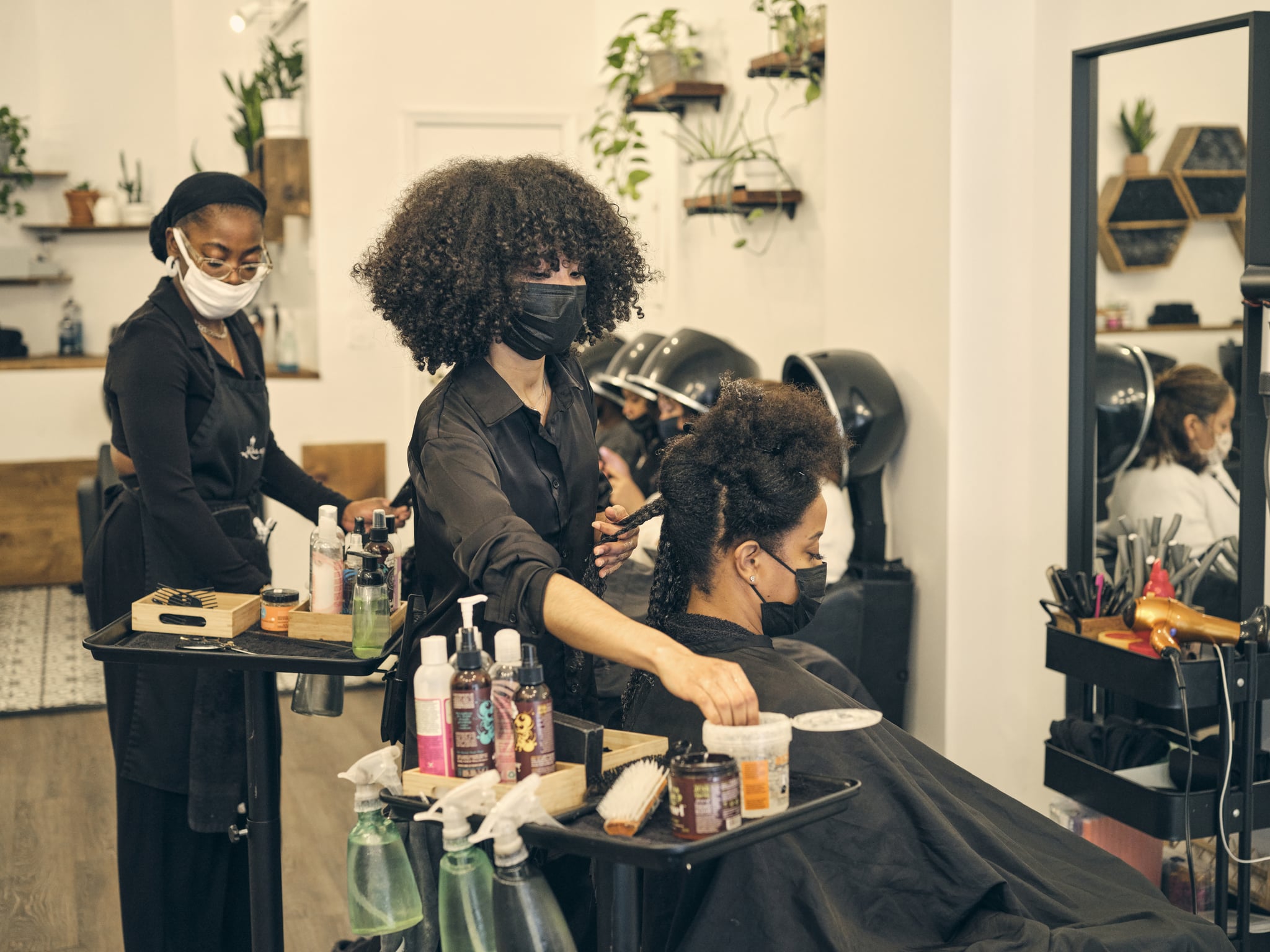 Женщина укладывает натуральные вьющиеся волосы клиента в салоне